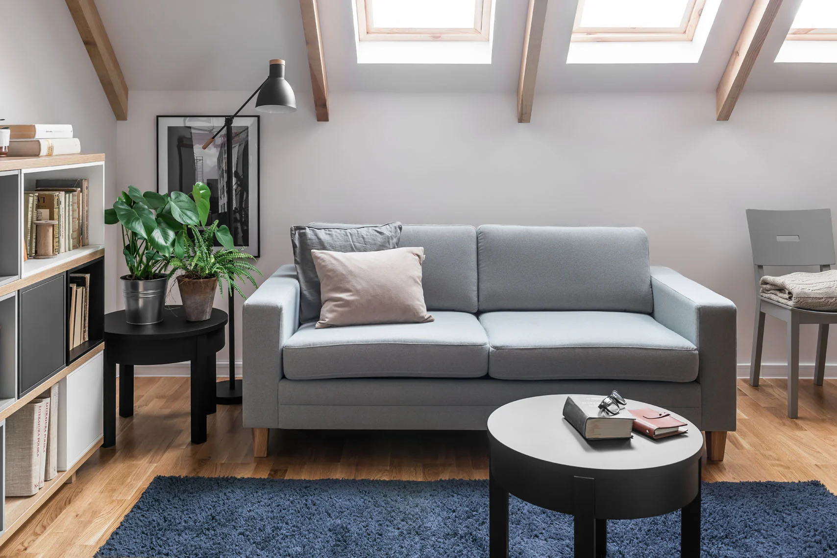Szara sofa w pokoju na poddaszu z oknami dachowymi i roślinami zapewnia efekt przestrzeni i światła.